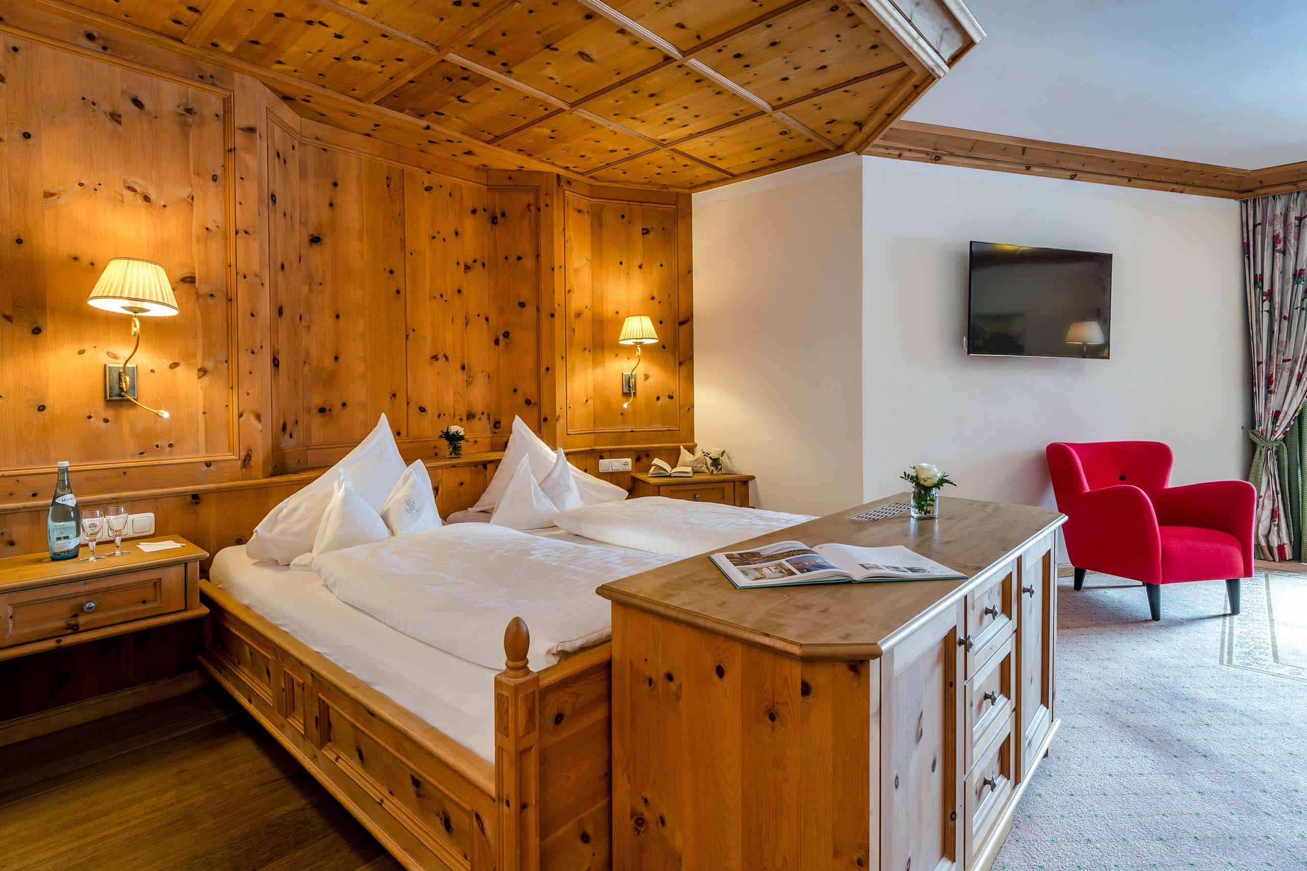 JuniorSuiteBSuperior3 Doppelbett vor Holzwand und Holzdecke, mit Holzkasten davor