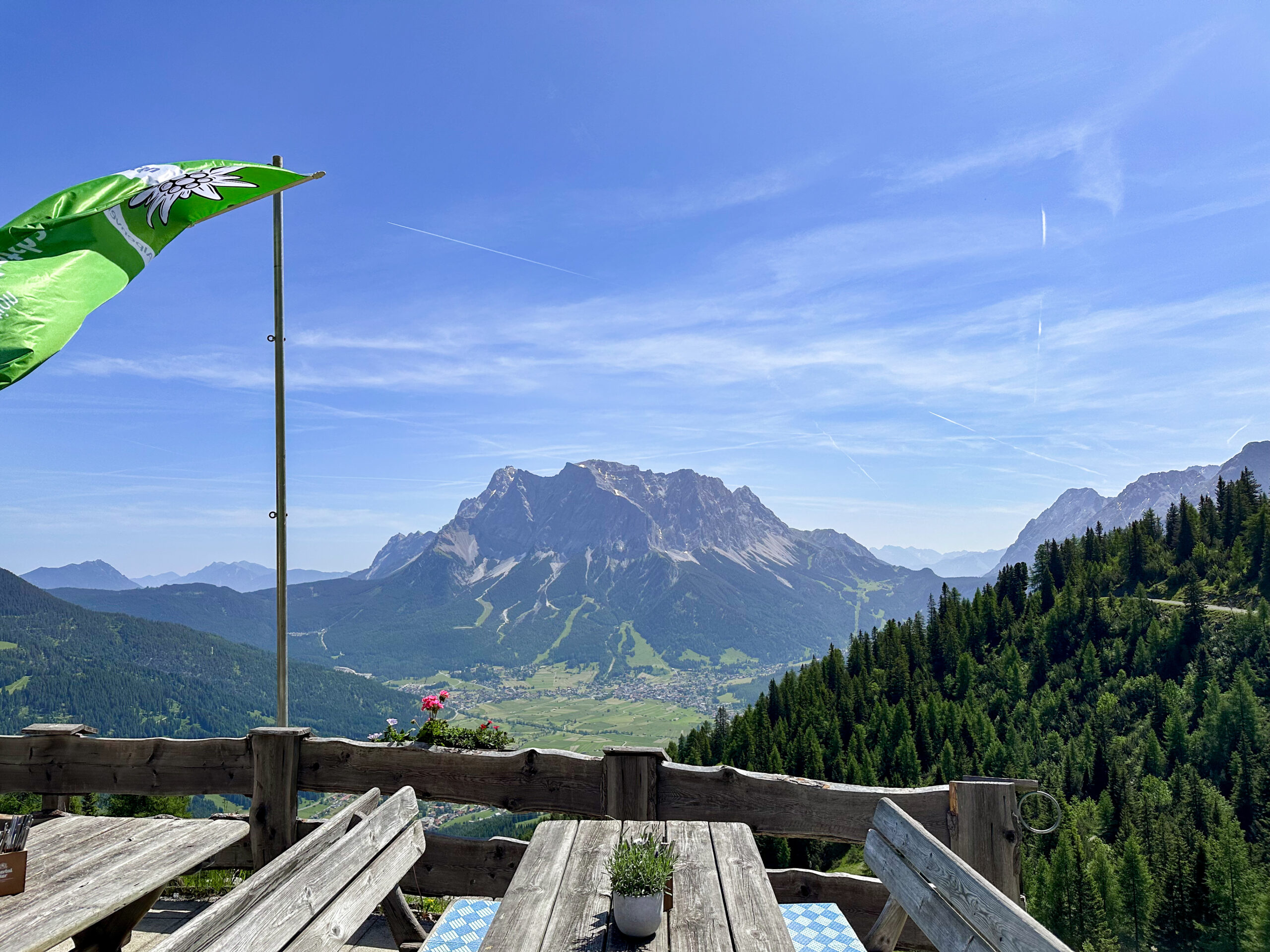Holztische und Bänke mit wehender Fahne und Blick ins Tal und auf gegenüberliegenden Berg